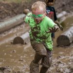 Boy competing in a mud run at Three Creeks strikes a Heisman Trophy-like pose