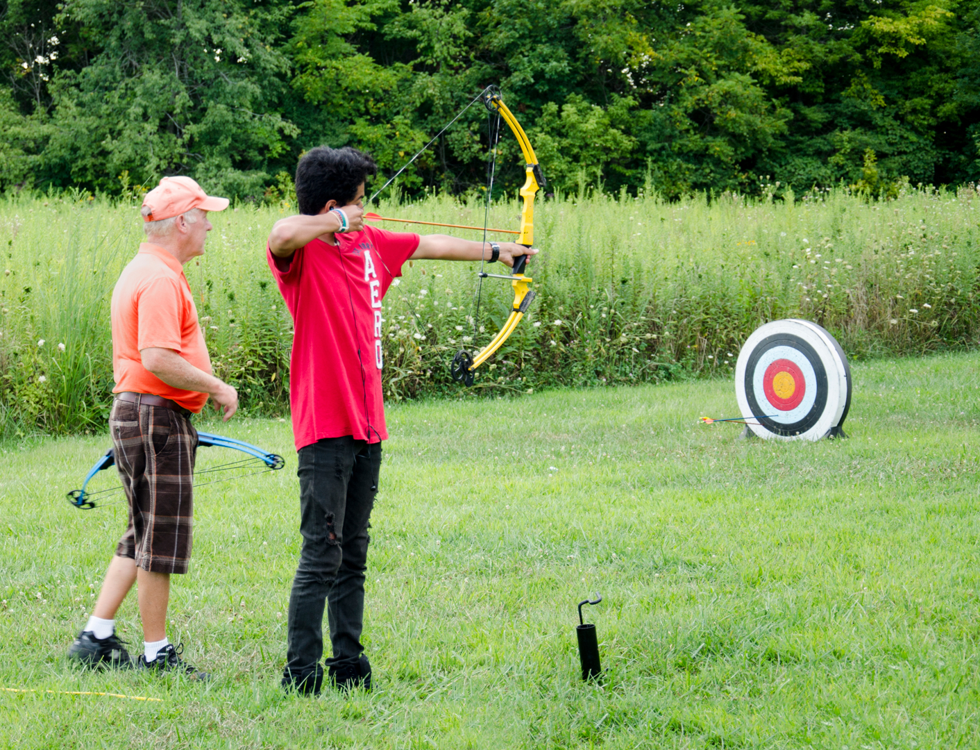 A boy shoots a compound bow at a target, supervised by a volunteer at Battelle Darby Creek Metro Park.