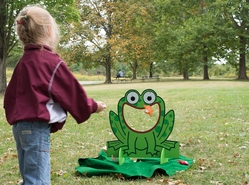 Girl at Blacklick Woods Creek Celebration tries to throw a cushion through the laughing frog's mouth.